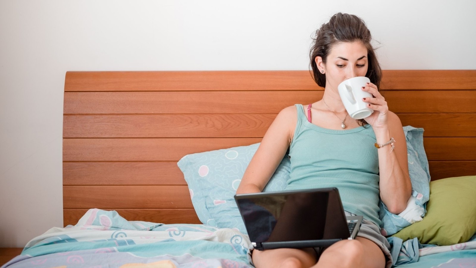 Image of a woman sitting in bed drinking coffee and using a laptop. This image represents how easy online therapy in Tennessee is. Those looking for an online therapist in Nashville, TN should check out Jody Dianna. | 37212 | 37129