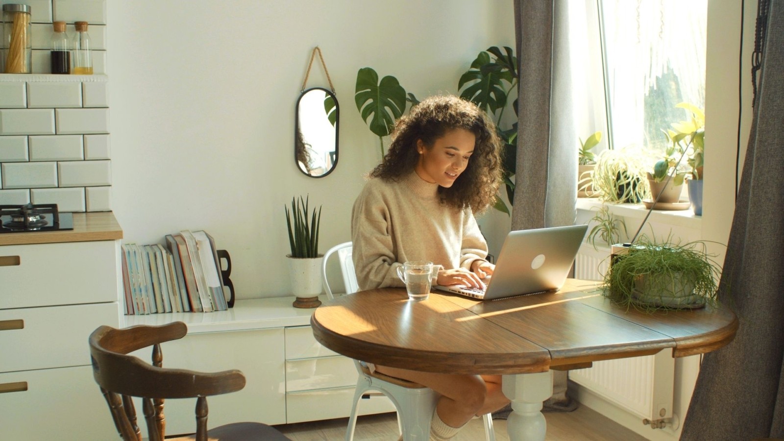 Image of a young woman sitting at a kitchen table and using a laptop. This image depicts what a college student meeting with an online therapist in Nashville, TN may look like. And anybody in the state can use online therapy in Tennessee. | 37129 | 37204