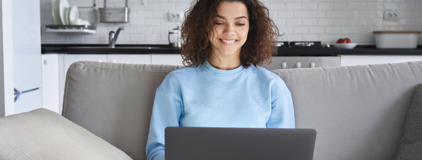 Image of a young woman using a laptop and smiling. This image represents how anxiety treatment in Nashville, TN can help decrease college student anxiety. | 37130 | 37916
