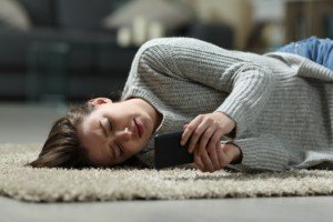 Image of a young woman lying on the floor and looking at her phone. This image depicts how college students with anxiety may cope before meeting with an anxiety therapist in Nashville, TN for anxiety treatment. | 37205 | 37204
