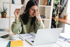 Image of a young woman sitting at a computer and pinching her nose. This image illustrates what a college student with anxiety symptoms may look like before meeting with an anxiety therapist. Try anxiety treatment in Nashville, TN to find relief. | 37205 | 37204