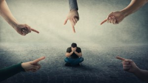 Image of a man sitting on the floor with his hands covering his face with fingers pointing at him. This image illustrates the social pressure college students feel before starting anxiety treatment in Nashville, TN. 37212 | 37215